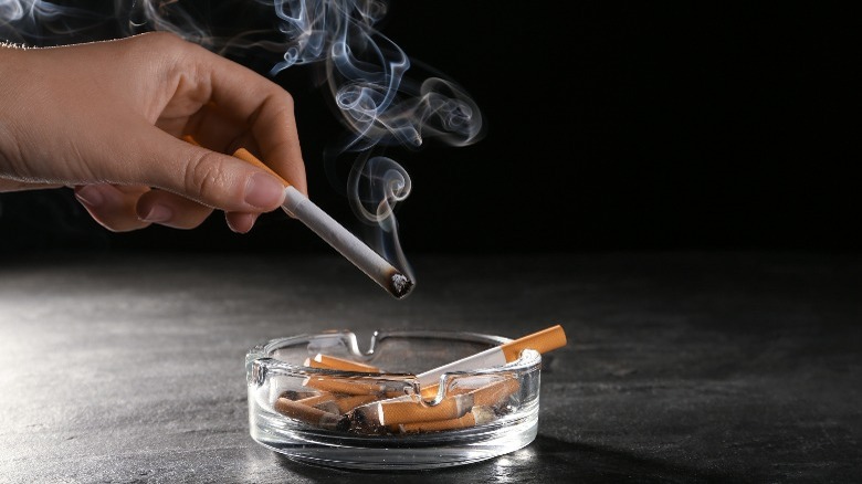 Ashtray with cigarette butts and hand holding cigarette
