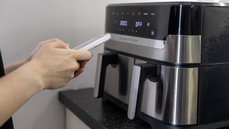 Person using a smartphone to program an air fryer