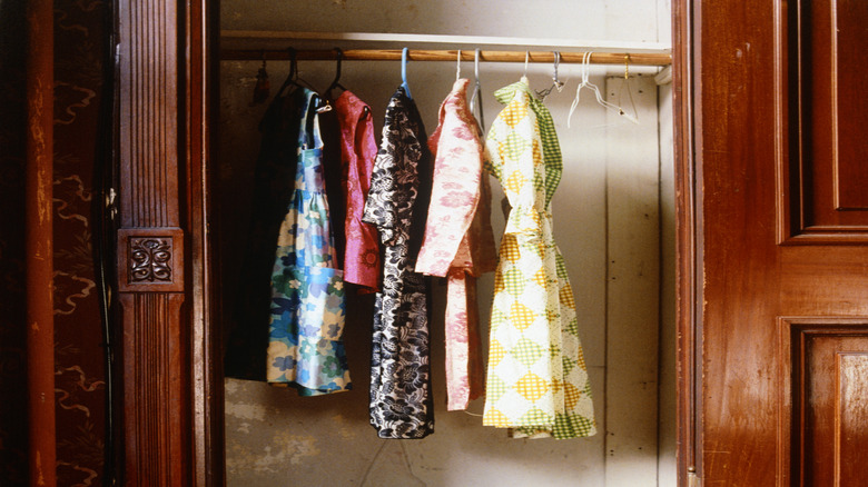 An old closet with vintage dresses hanging inside and the doors removed.