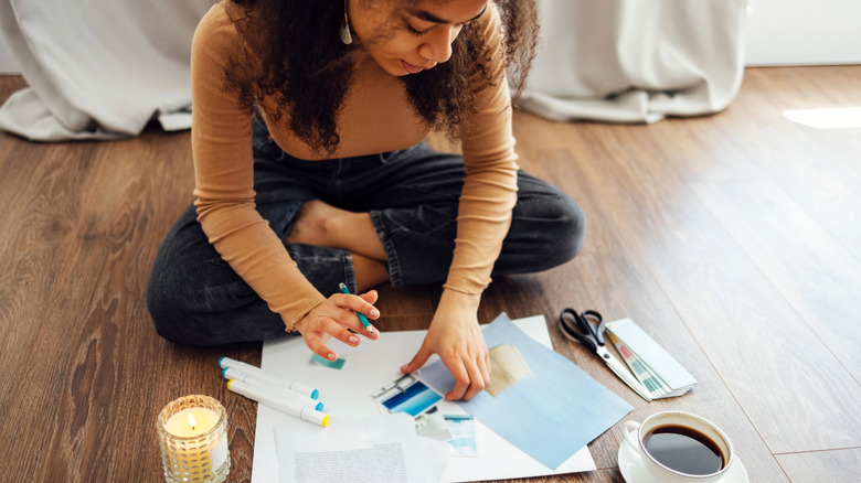 A young woman sits on the floor and works on paper crafts.