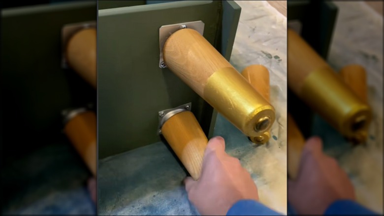 A person attaches wooden legs to a shelving unit made from drawers.