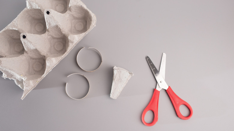 An empty egg carton cut up next to a pair of red scissors