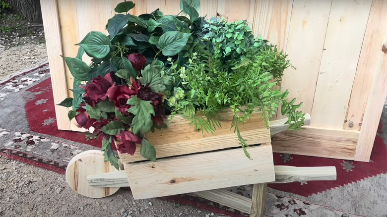 A rustic wheelbarrow planter crafted from repurposed old picket fences, brimming with lush, vibrant plants.