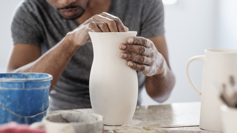 Man molding clay vase on table