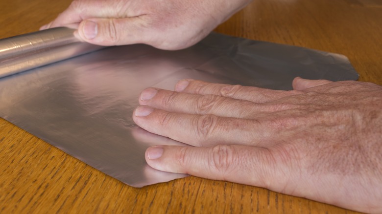 Hands unrolling aluminum foil