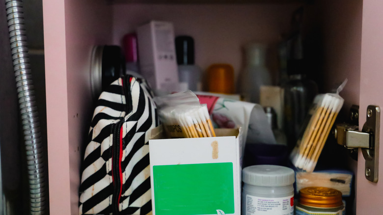 A messy dark bathroom cabinet is filled with toiletries