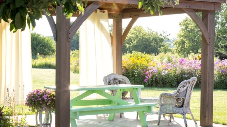 Garden gazebo with green picnic bench, two wicker chairs, and light curtains