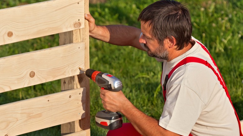 Man screwing wide slats to outdoor support post with cordless drill