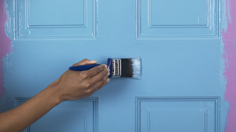 Hand painging over a pink door with blue paint