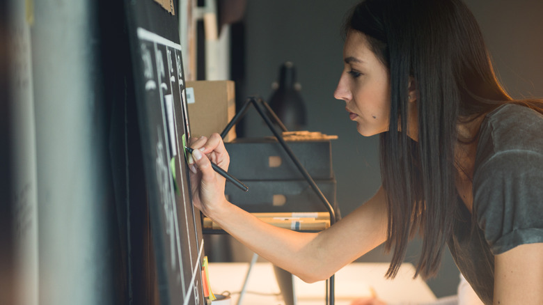 A woman writing on a chalkboard organization chart.