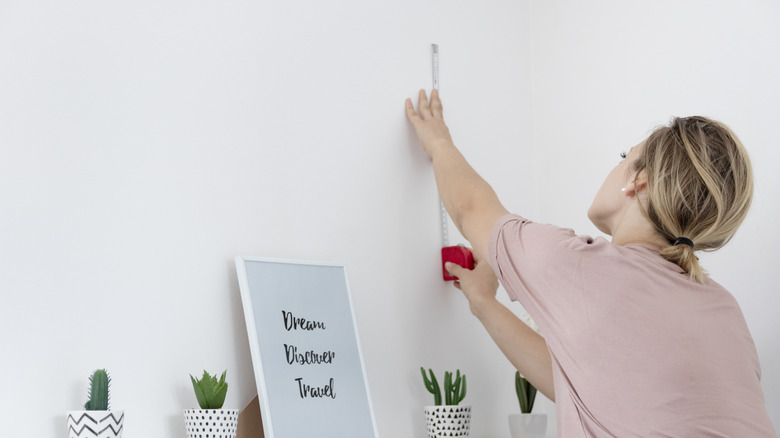 A woman holding a measuring tape to an empty wall.