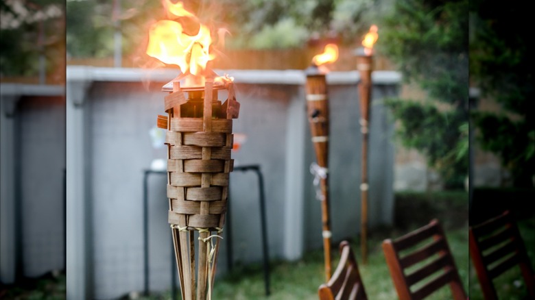 Tiki torches lined up in backyard behind chairs