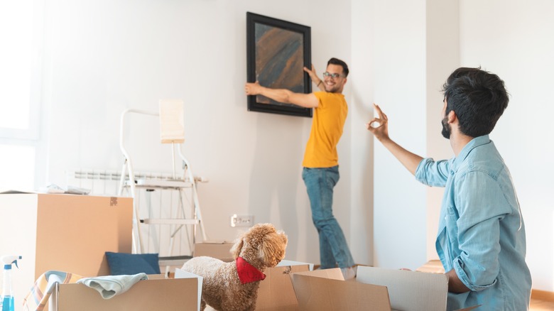 Two men hanging up a wall painting after recently moving