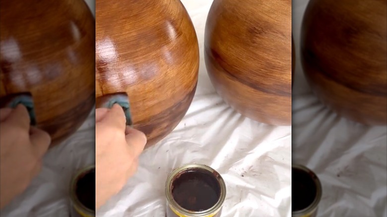 person putting dark stain on DIY spheres made from IKEA BLANDA bowls