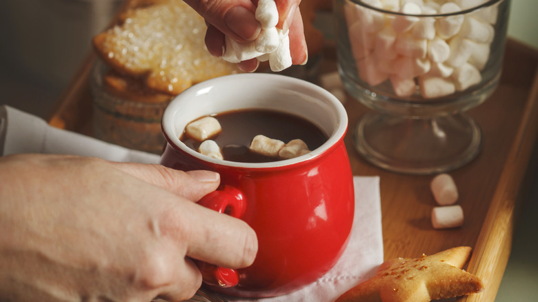 Hand adding marshmallows to a cup of hot cocoa