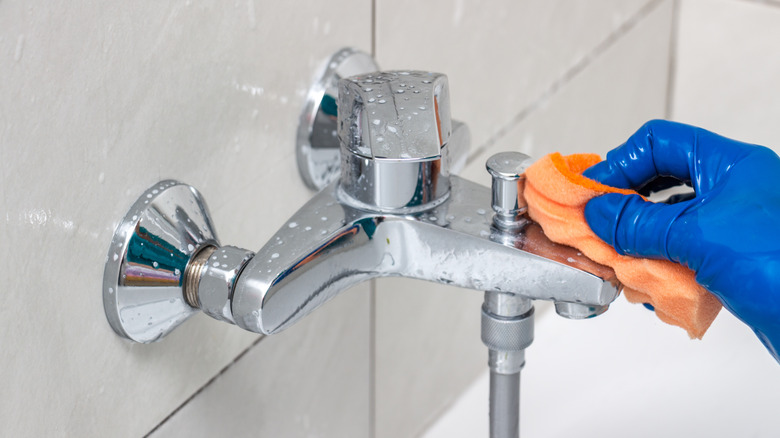 Person cleaning faucet with cloth