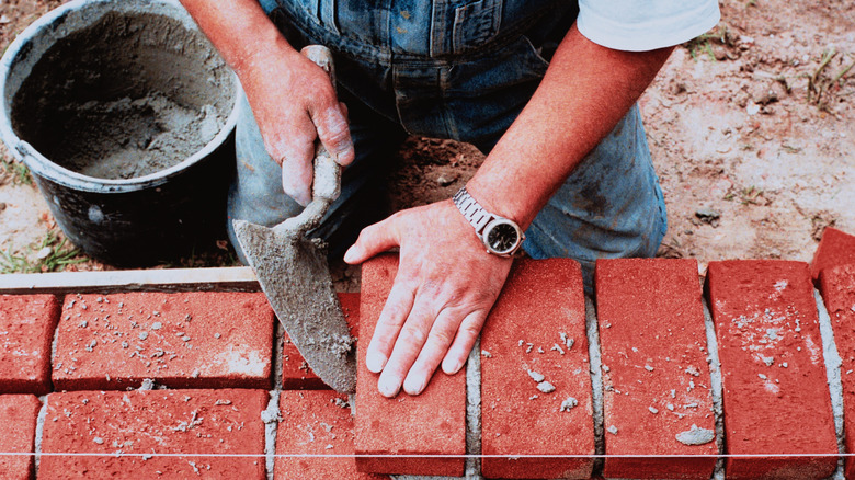 A man using mortar to build with red bricks.