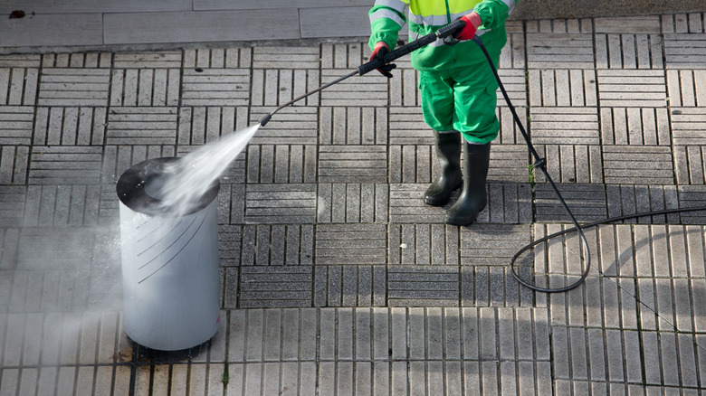 A worker cleans a city trash can with a pressure washer