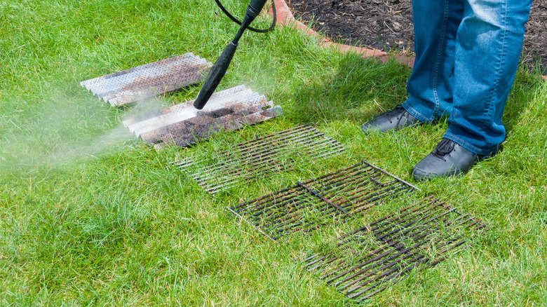 A pressure washer cleans grill grates in the grass