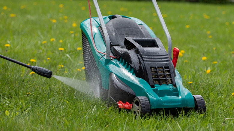 A pressure washer cleans a lawn mower