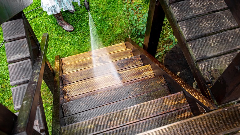 A person pressure washes wooden outdoor stairs 