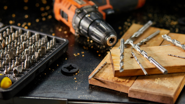 Drill and drill bits sitting on table with wood