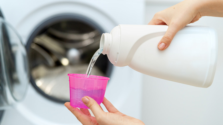 Person pouring liquid laundry detergent in front of washing machine.