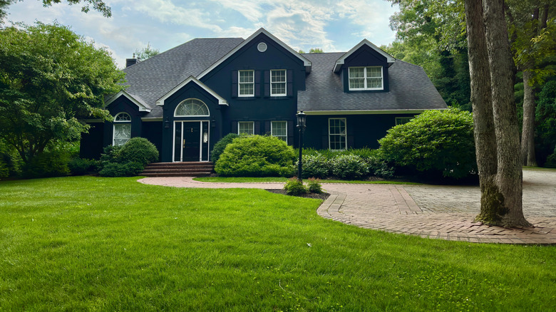 Front garden of a house with a luscious dark green lawn, shrubs and trees.