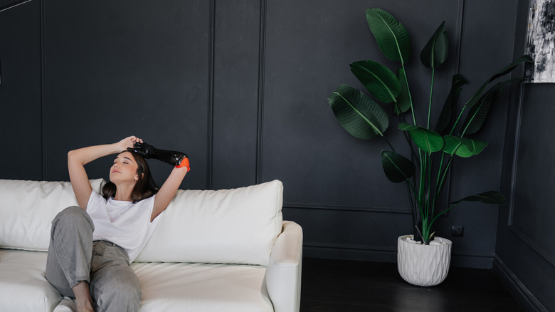 A woman sitting on a white couch in a room with dark walls and a corner plant.