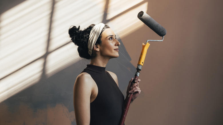 A woman holding a paint roller with black paint in an empty room.