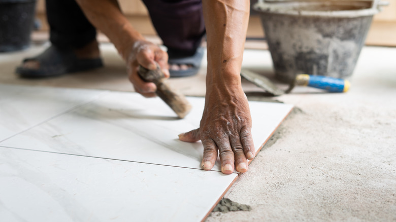 Person installing large white tile on floor