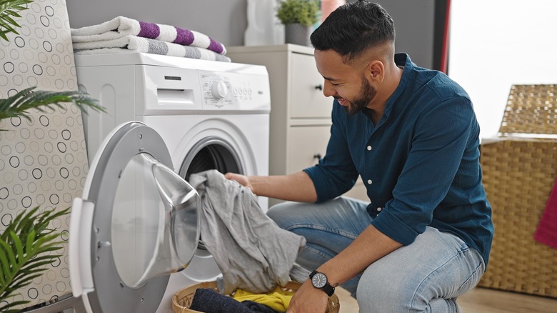 A man crouched in front of a washing machine with laundry