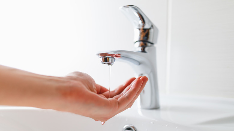 Hand catching trickle of water from low-pressure faucet