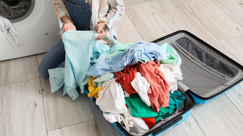 Loading a washing machine with stained clothes from a suitcase