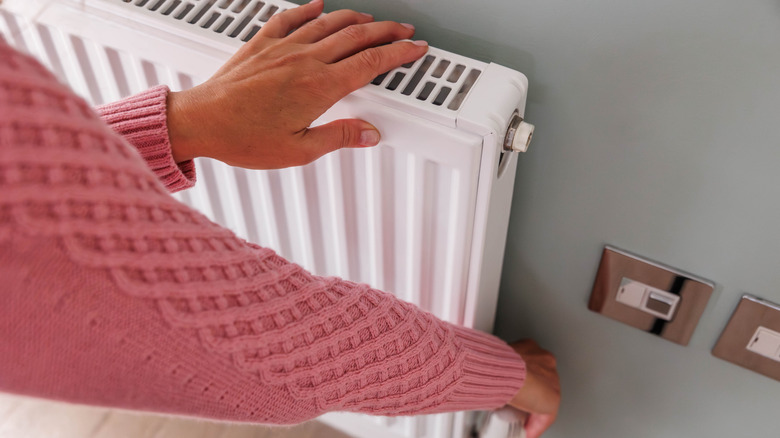 A person in a pink sweater adjusting the temperature on a wall-mounted heater