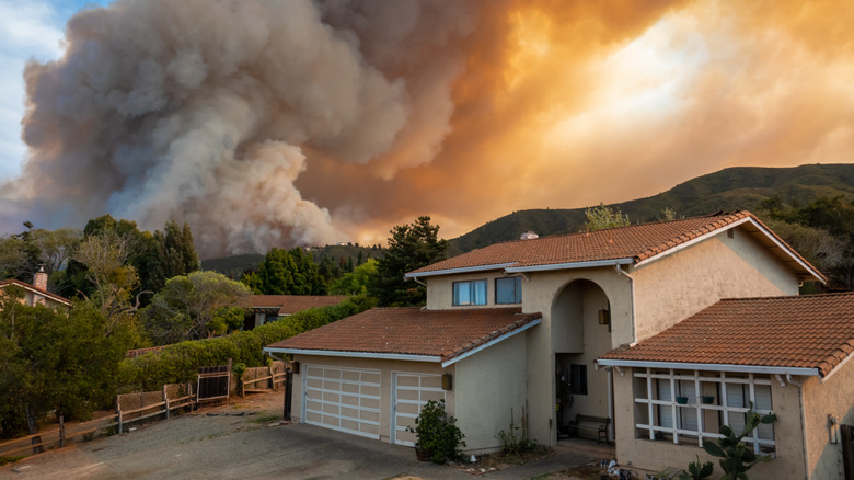 california wildfire and smoke behind untouched mediterranean house