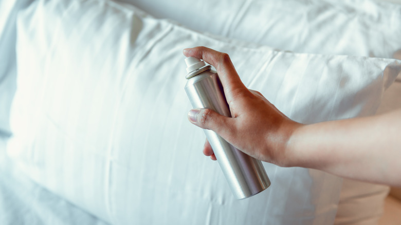 Hand sprays canister near pillows on bed