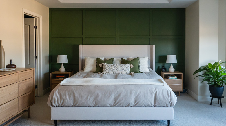 A bed with a green wall behind it in an interior designed bedroom