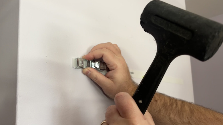 Hands hammering metal hardware into the wall