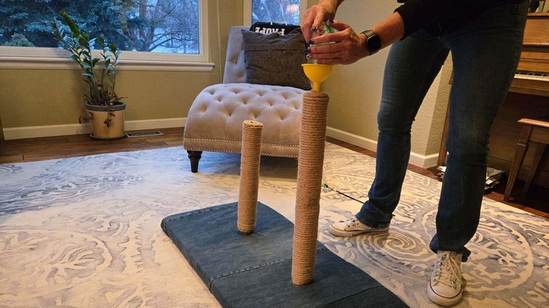 person using a funnel and a stick to fill post with catnip