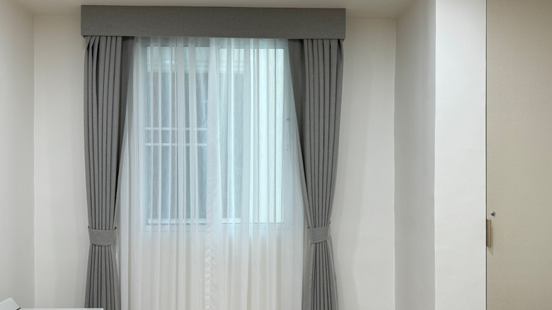 Grey decorative drapes layered over translucent white curtains