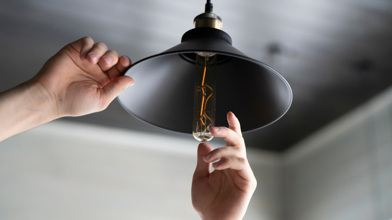 A pair of hands changing a lightbulb on a black hanging lamp