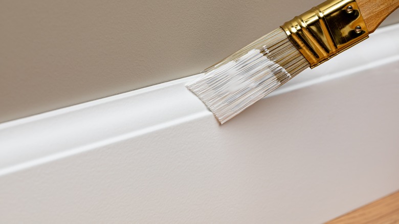 Person painting a baseboard with white paint