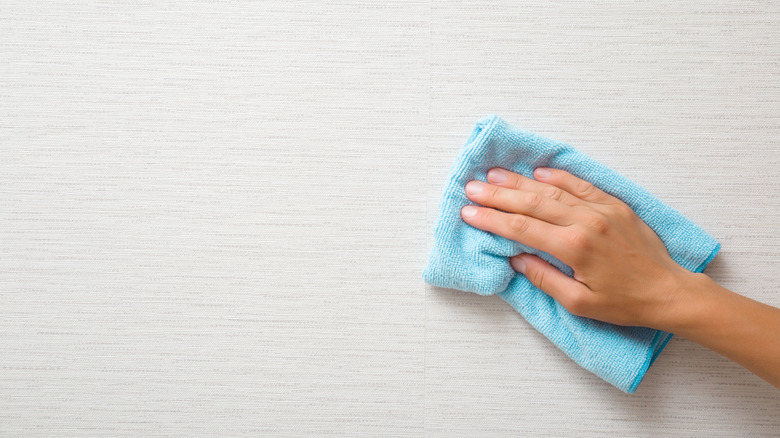 Person cleans textured wallpaper with microfiber cloth