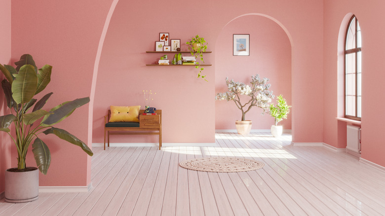 A dusty pink room features arches, a white wood floor, and natural wood accessories