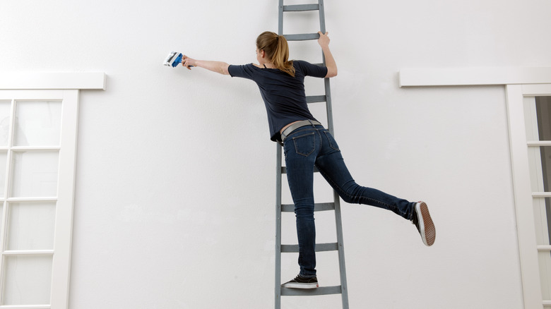 woman painting wall from ladder