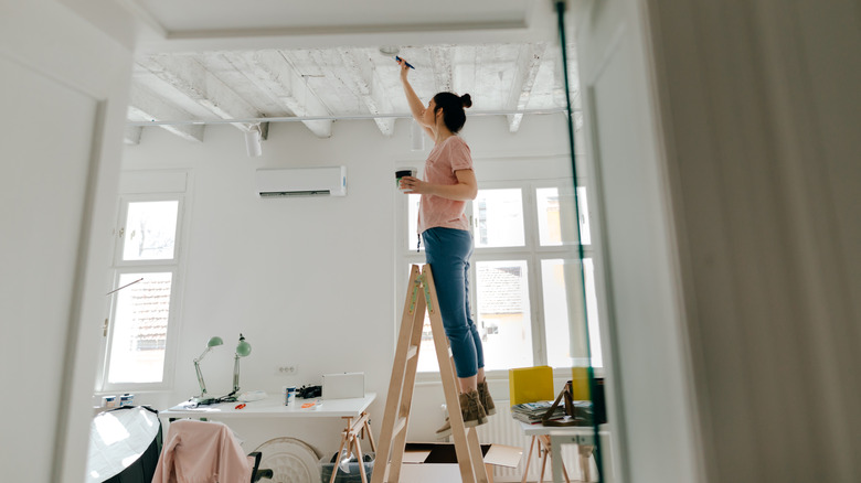 woman painting ceiling on ladder
