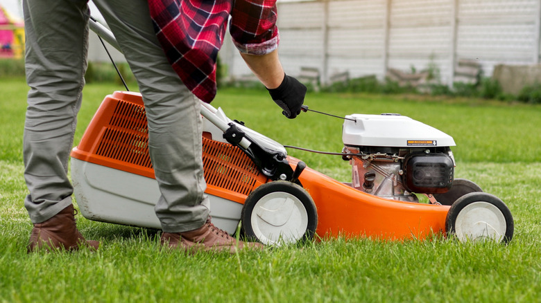 A persona starting a lawnmower with pull start