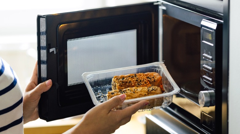 Woman putting egg rolls in plastic container into microwave oven