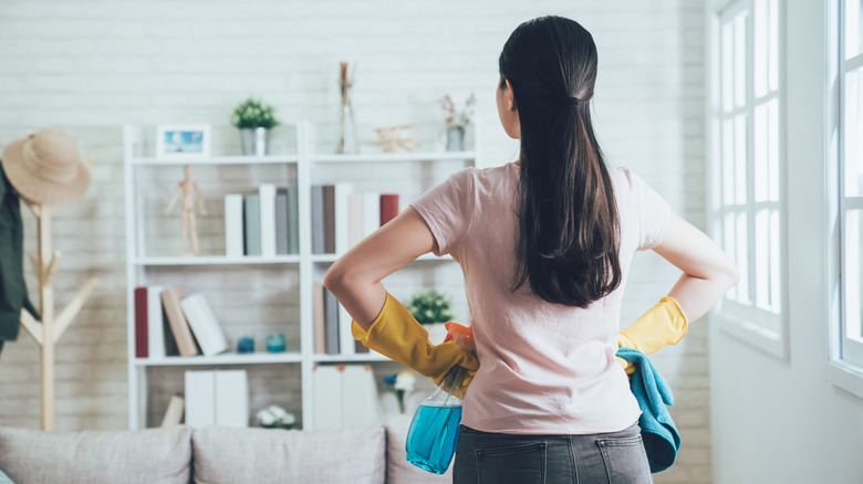 Backview of woman in living room with gloves and cleaning products